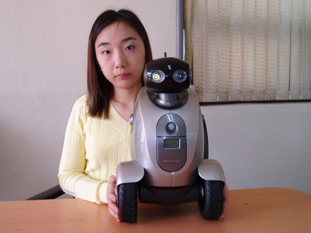 A camera and motion sensor-installed home robot is shown in its actual configuration. A new concept in Home Network Services that lets customers constantly monitor the entire conditions at their house, on a real-time basis through a moving robot, is scheduled to be launched by the first part of this year.